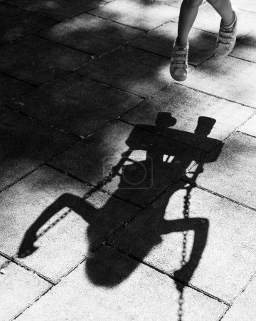 La silhouette et l'ombre de l'enfant se balancent dans une balançoire pour tout-petits dans une aire de jeux. Les enfants jouent en extérieur