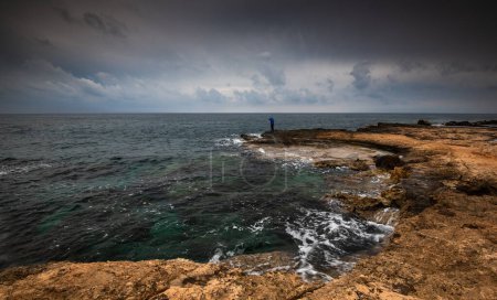 Photo for Man standing alone at the edge of rocky beach in Stormy Weather. Cape Greko Cyprus. - Royalty Free Image