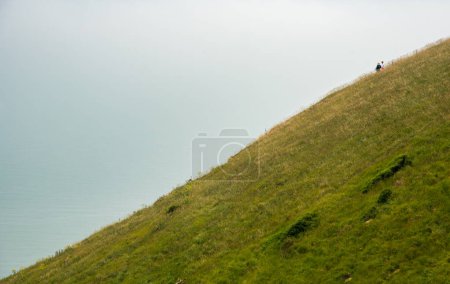 People hiking at the edge of a green cliff along the ocean at mist. People active outdoors. Healthy life style. Beachy head United Kingdom