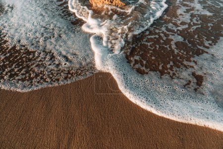 Directly above view of waves breaking on shore at sunset. stone, waves, foam.