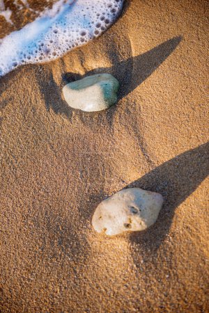Sand und Steine am Meer, Wellen am Strand bei Sonnenuntergang