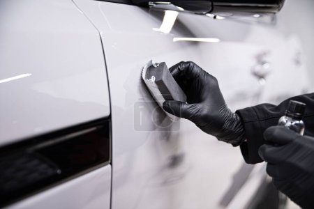 Mitarbeiter einer Autowaschanlage oder eines Autodetailstudios tragen eine Keramikbeschichtung auf ein weißes Auto auf