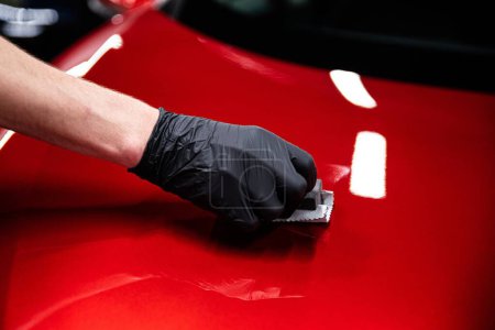 Foto de Empleado de un estudio de lavado de coches o detalles del coche aplica un recubrimiento de cerámica a la pintura de un coche rojo - Imagen libre de derechos