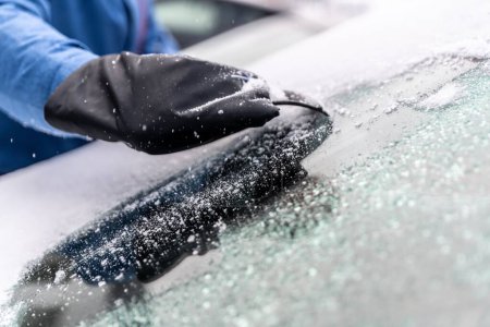 Téléchargez les photos : L'homme utilise des grattoirs à glace pour dégeler un pare-brise de voiture recouvert de glace - en image libre de droit