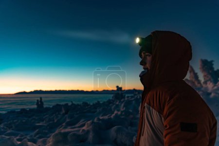 Teenager in warmer Winterjacke mit Stirnlampe auf einem Winterwanderweg in den Bergen. Minuten vor Sonnenuntergang, Babia Gora, Beskiden, Polen