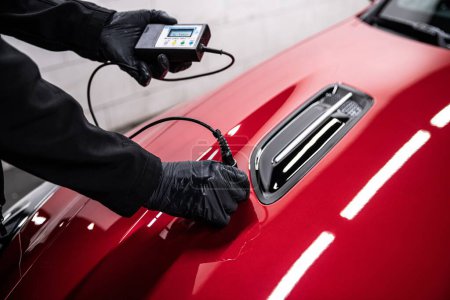 Foto de Employee of a car service checks the thickness of the paint coating of a red car - Imagen libre de derechos