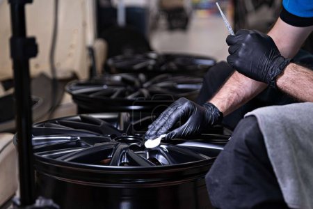 Téléchargez les photos : Employee of a car detailing studio applies a protective ceramic coating to a car rim - en image libre de droit