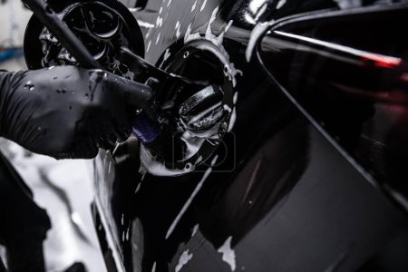  Car detailing studio or car wash employee cleans the fuel filler area of a black car with a special brush.