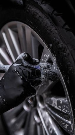 Foto de Empleado del estudio de detalles del coche o lavado a mano limpia a fondo una rueda de coche de aluminio con un cepillo - Imagen libre de derechos
