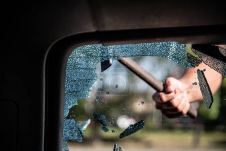 Foto de Ladrón de coches rompe la ventana del coche con un martillo - Imagen libre de derechos