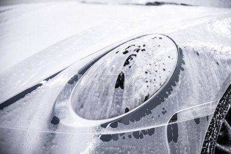 Foto de Frente a un coche deportivo gris y la luz delantera están cubiertos con espuma activa utilizada en los estudios de detalles del coche - Imagen libre de derechos