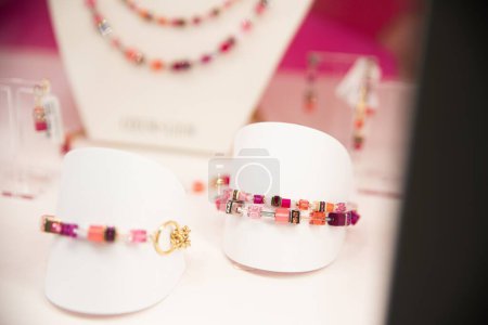 Foto de Pulsera de piedras preciosas de colores en pantalla blanca con pendientes borrosos en el fondo, con fondo rosa. - Imagen libre de derechos
