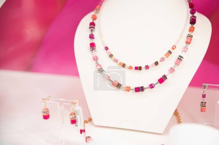 Foto de Collar de piedras preciosas de doble hebra y pendientes a juego en un soporte de exhibición blanco con un fondo rosa vibrante - Imagen libre de derechos