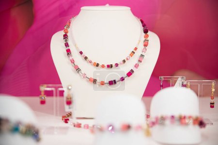 Foto de Collar de piedras preciosas de doble hebra y pendientes a juego en un soporte de exhibición blanco con un fondo rosa vibrante - Imagen libre de derechos