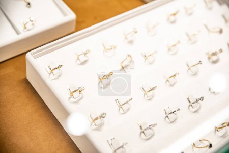 Foto de Array de anillos brillantes que se muestran en una bandeja blanca con ranuras individuales, mostrando varios diseños, algunos con bandas de oro y diamantes - Imagen libre de derechos