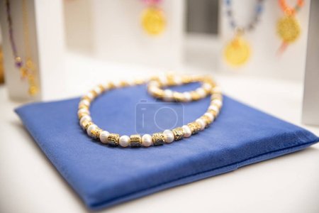 Foto de Collar de perlas y cuentas de oro en un paño azul contra una pantalla de joyería borrosa - Imagen libre de derechos
