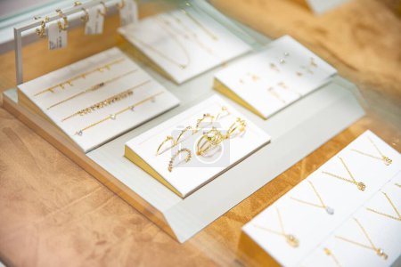 Foto de Elegante exhibición de varias piezas de joyería de oro, incluyendo collares, pendientes y anillos, exhibidos en soportes blancos - Imagen libre de derechos
