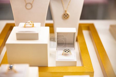 Foto de Anillo de oro con piedras preciosas de colores presentado en un cojín blanco con un fondo borroso de exhibición de joyas - Imagen libre de derechos