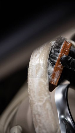 Foto de El empleado de lavado de coches o un estudio de detalles de automóviles limpia a fondo un volante de cuero ligero con un cepillo y detergente - Imagen libre de derechos