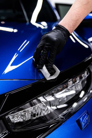 Foto de Trabajador del estudio o del lavado del coche que detalla del coche que aplica el recubrimiento del coche de cerámica en capucha azul del coche - Imagen libre de derechos