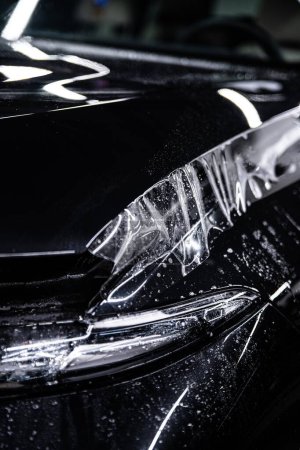 Foto de Coche negro protegido con película de protección de pintura PPF transparente en un estudio de detalles de automóviles - Imagen libre de derechos