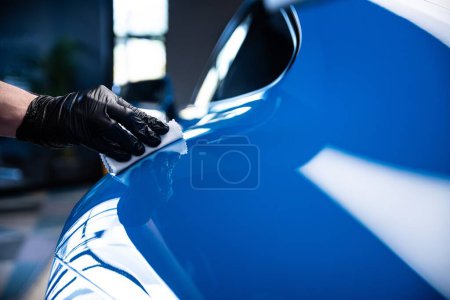Foto de Coche efectivo o coche detallando trabajador de estudio aplicando grafeno o recubrimiento de cerámica en coche deportivo azul. - Imagen libre de derechos