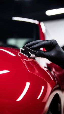 Foto de Trabajador de estudio de detalle de coche aplicando cuidadosamente recubrimiento de cerámica en coche rojo - Imagen libre de derechos