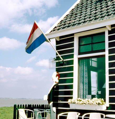 Foto de URK, HOLLAND-AGOSTO 08,2022: Pequeño café con bandera holandesa y camarero de madera en la frontera del IJselmeer - Imagen libre de derechos