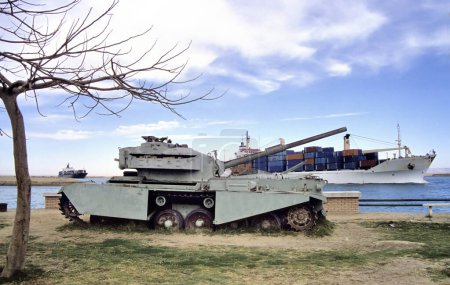 Téléchargez les photos : Vieux char blindé rouillé le long du canal de Suez en Egypte avec passage de porte-conteneurs à l'arrière-plan - en image libre de droit