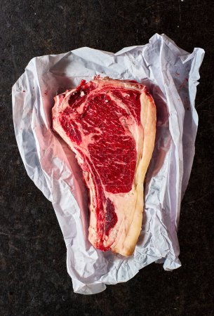 Téléchargez les photos : Steak basque Txuleton ou steak côtelé Premier Bone-in enveloppé dans du papier boucher, placé sur un fond de marbre noir. - en image libre de droit