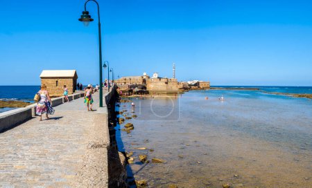 Photo for Cadiz, Spain - August 1, 2023. People enjoying a sunbathing in La Caleta beach, with the San Sebastian Castle, a fortress in La Caleta island, in the background. View from Paseo Fernando Quinones Promenade. Cadiz. Andalusia, Spain. - Royalty Free Image