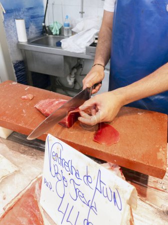 Photo for A fishmonger cutting slices from a piece of Red Tuna in a fish shop in a Spanish market. Cadiz, Andalusia, Spain. - Royalty Free Image
