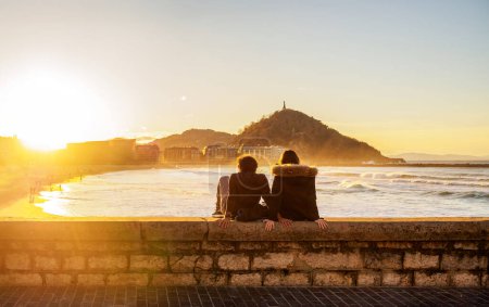 Photo for A young couple enjoying Zurriola Beach at sunset with Monte Urgull in the background. San Sebastian, Basque Country, Guipuzcoa. Spain. - Royalty Free Image