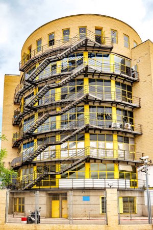 Un antiguo edificio industrial con prominentes escaleras de emergencia y grandes ventanas amarillas, mostrando su diseño arquitectónico histórico.