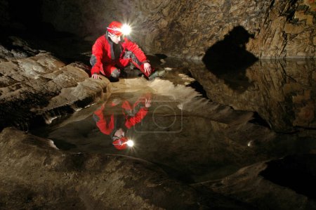 Spiegelbild eines Höhlenforschers in einem Höhlenwasserbecken. Carbid-Acetylen-Gaslampe am Helm beleuchtet den Untergrund