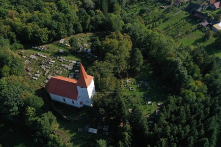 Luftaufnahme einer weiß getünchten Kirche und eines Friedhofs. Drohnenaufnahme eines mittelalterlichen Wahrzeichens in Bikfalva, Bicfalau, Szeklerland, Rumänien