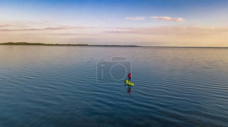 Foto de Woman paddling on SUP board on beautiful lake aerial drone view with reflections from above. Standing up paddle boarding adventure in early morning sunrise. Germany lake district Mecklenburg. - Imagen libre de derechos