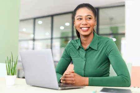 Téléchargez les photos : Attractive young african-american freelancer woman in green casual shirt working on laptop in coworking space, enjoying remote work and free work schedule - en image libre de droit