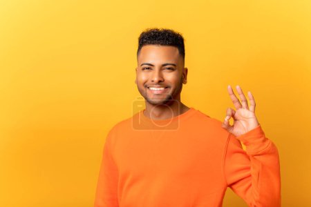 Foto de Everything is fine. Satisfied Indian man showing ok gesture with hand, approving work, satisfied with quality. Indoor studio shot isolated on yellow background - Imagen libre de derechos