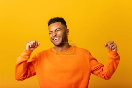 Foto de Extremely excited overjoyed indian man shouting making yes gesture, amazed with his victory, triumph. Indoor studio shot isolated on yellow background - Imagen libre de derechos