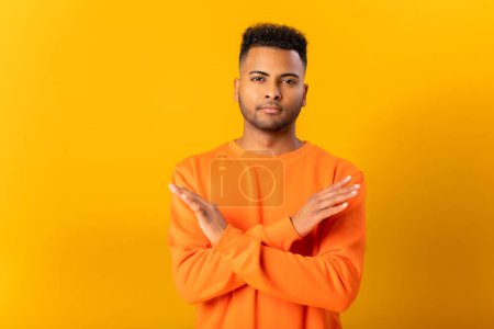 Photo for Indian guy denies, holding hands crossed in sign of disagreement, decline, shows no with gestures, arab man demonstrates rejection expresion, studio shot isolated on yellow - Royalty Free Image