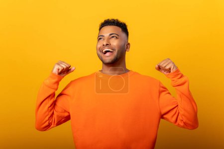 Téléchargez les photos : Handsome overjoyed crazy happy Indian guy screaming yes in ecstatic, raising fists up, celebrating good luck, victory, isolated on yellow. Goal achievement concept - en image libre de droit