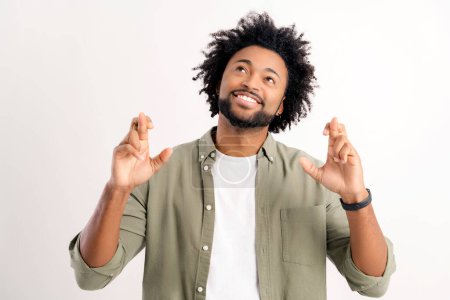 Téléchargez les photos : Attractive curly handsome young guy holding fingers crossed isolated on white, charismatic african-american man wishing something, making good luck sign, dreaming, desire - en image libre de droit