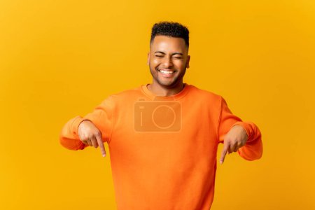 Foto de Here and now. Handsome man pointing finger down, laughing facial expression. Indoor studio shot isolated on orange background - Imagen libre de derechos