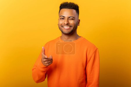 Téléchargez les photos : Portrait d'homme portant un pull orange de style décontracté, pointant du doigt pistolet à la caméra ludique et flirtant, choisissant gagnant chanceux. Studio intérieur tourné isolé sur fond orange - en image libre de droit