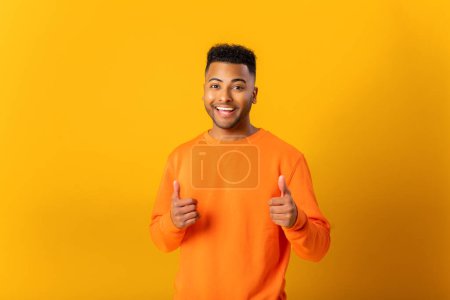 Téléchargez les photos : Portrait of man wearing orange casual style sweater, pointing finger pistols to camera playfully and flirting, choosing lucky winner. Indoor studio shot isolated on orange background - en image libre de droit