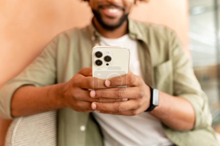 Photo for Cropped view of the young African-American man hands sitting at chair, surfing Internet on his mobile phone, working on social media projects, checking emails, and chatting with friends - Royalty Free Image