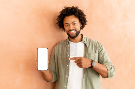 Photo for African American man standing isolated over the wall background, presenting new application, pointing with hands on mobile phone with white blank space for advertisement, mockup image - Royalty Free Image