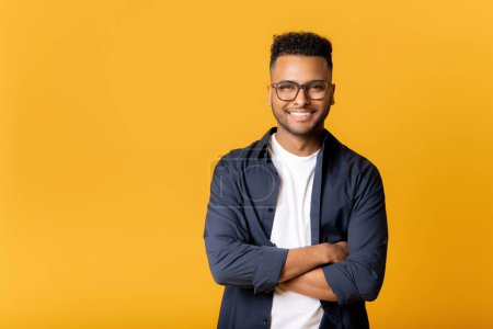 Photo for Portrait of successful indian man standing in confident pose with arms crossed and looking at the camera isolated on yellow, cheerful male entrepreneur, freelancer smiling - Royalty Free Image