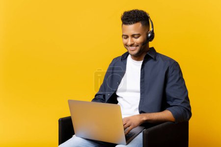 Foto de Hombre indio concentrado con auriculares celebración de videoconferencia virtual sentado en la silla con un ordenador portátil en las vueltas, chico que estudia en línea, webinar involucrado - Imagen libre de derechos